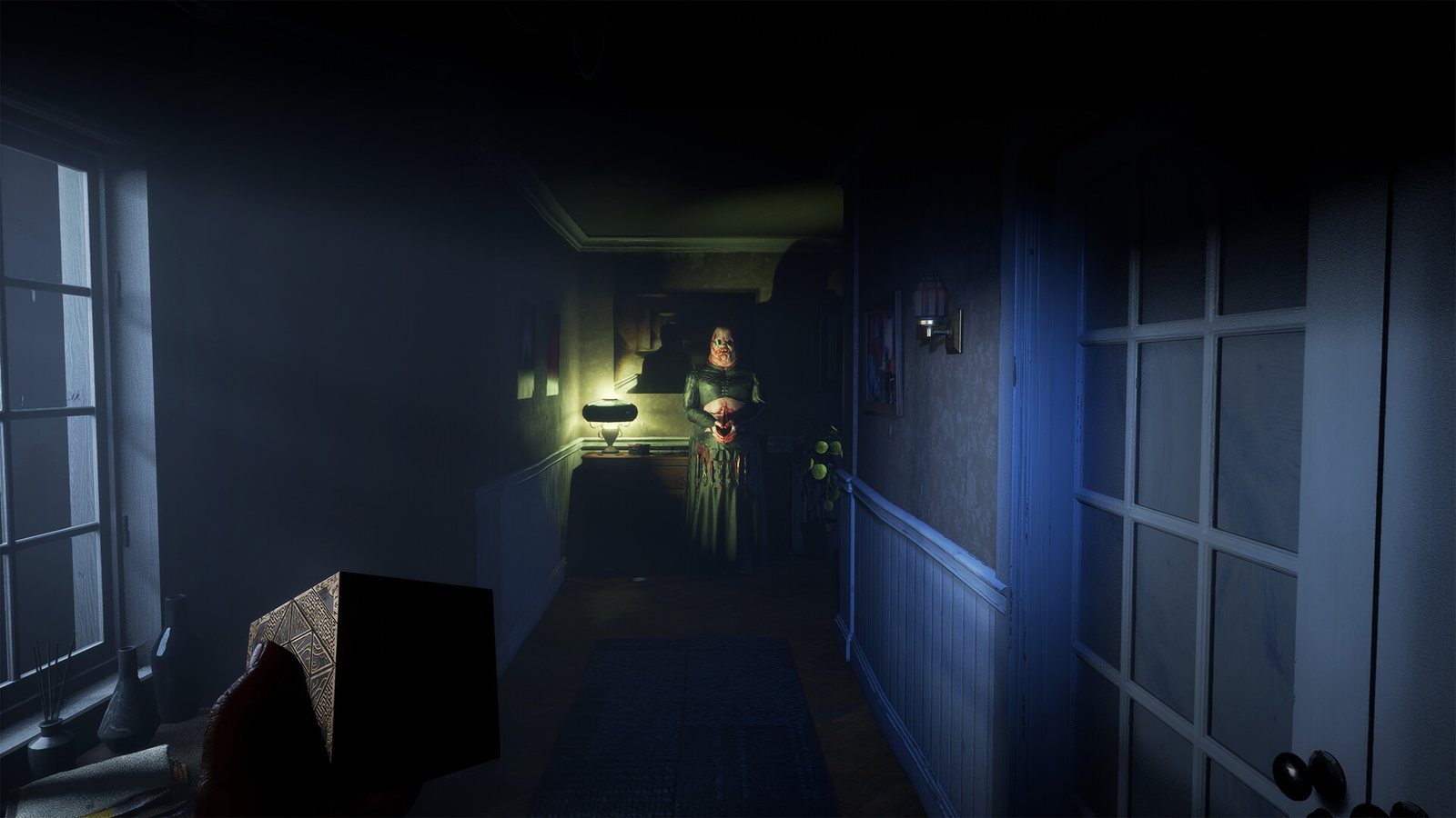 A woman in a green dress at the end of a dim apartment hallway