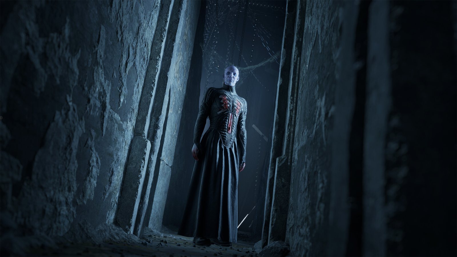 A pale robed figure with a red-lit grille on the chest, at the end of a narrow stone corridor. Official screenshot. A tall pale figure in a long dark robe with a red-lit grille on the chest blocks a narrow stone corridor