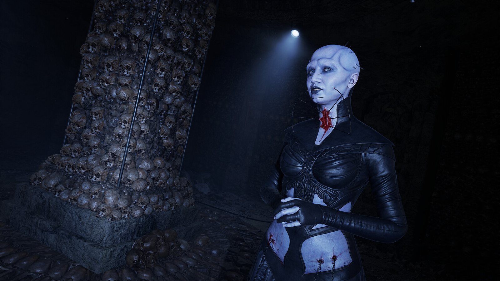 A pale woman in black leather beside a pillar studded with skulls, a red wound at her throat. Official screenshot. A pale woman in a black leather outfit stands beside a pillar studded with skulls