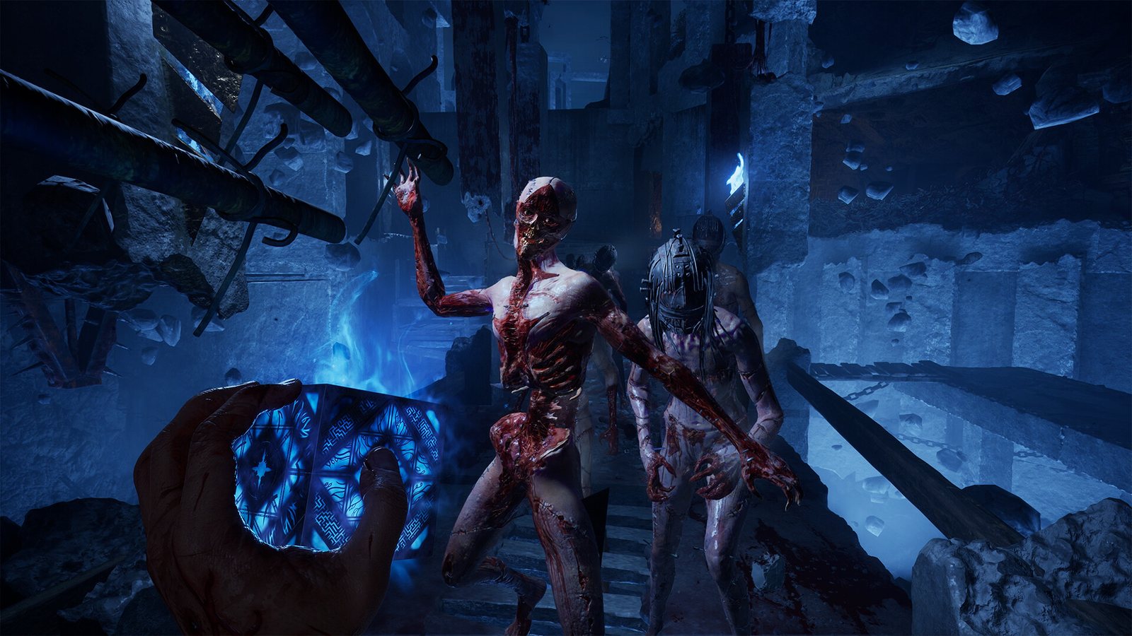 The glowing blue box held in one hand as bloodied figures advance through a ruined, chain-hung chamber. Official screenshot. Bloodied figures advance through a ruined chain-hung chamber as the blue box glows